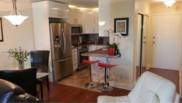 kitchen with stainless steel appliances, white cabinets, decorative light fixtures, and light wood finished floors