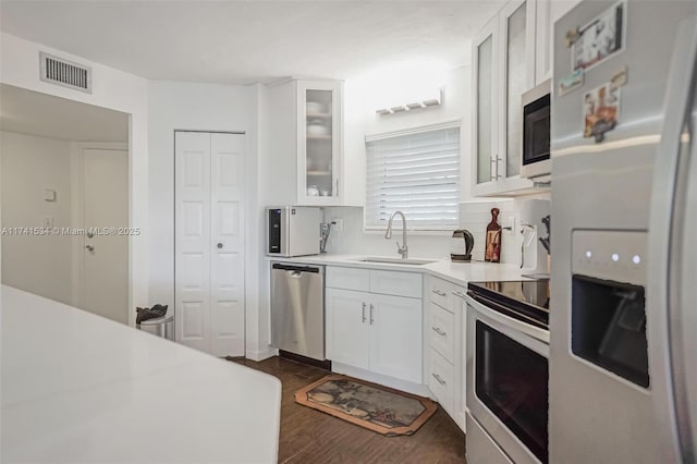 kitchen with light countertops, appliances with stainless steel finishes, glass insert cabinets, white cabinets, and a sink