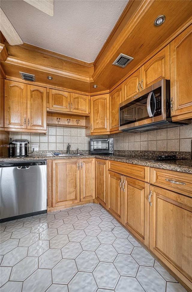 kitchen featuring sink, backsplash, dark stone counters, and appliances with stainless steel finishes