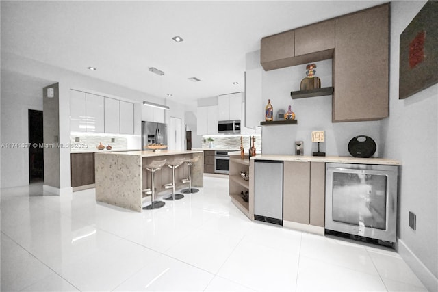 kitchen with a breakfast bar, an island with sink, white cabinetry, beverage cooler, and stainless steel appliances