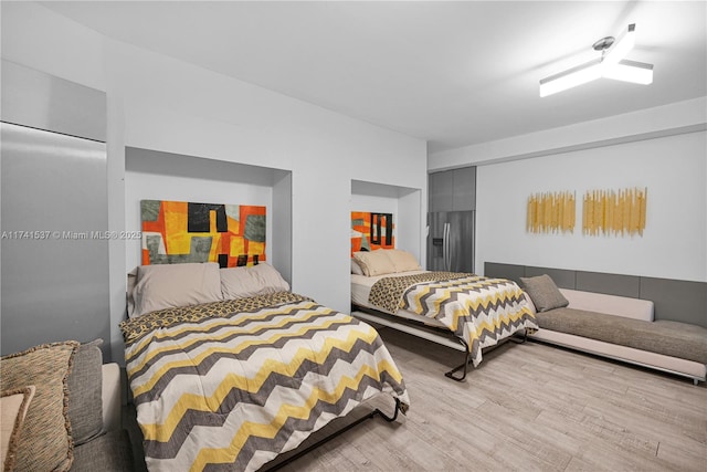 bedroom featuring stainless steel fridge and light hardwood / wood-style floors