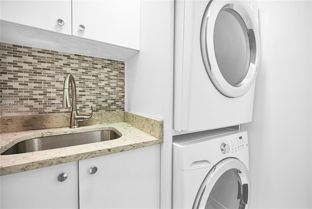 washroom featuring cabinets, stacked washer / dryer, and sink