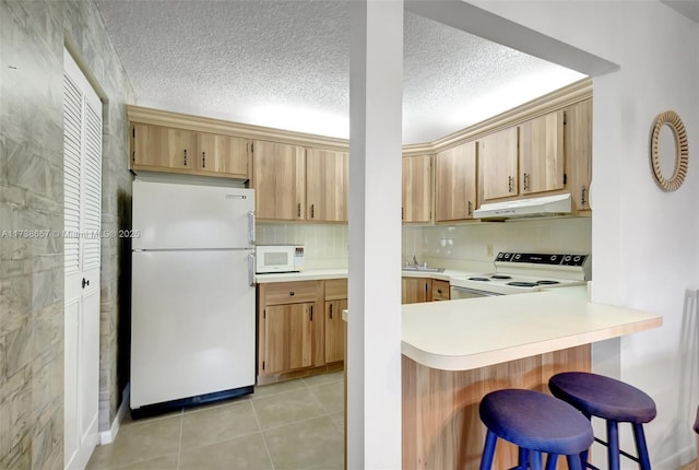 kitchen with white appliances, a breakfast bar area, a textured ceiling, light tile patterned flooring, and decorative backsplash