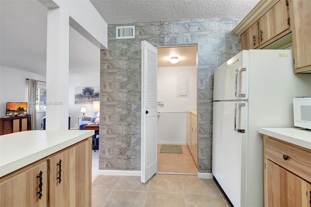 kitchen with light tile patterned flooring, light brown cabinets, a textured ceiling, and white appliances