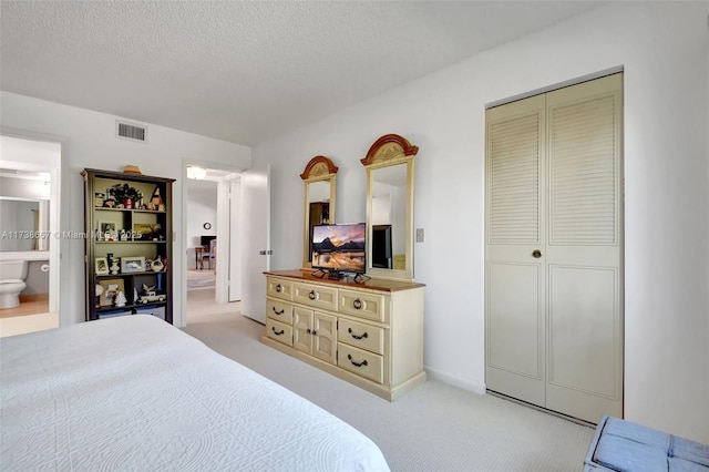 bedroom featuring a closet, ensuite bathroom, light carpet, and a textured ceiling