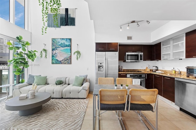 kitchen featuring stainless steel appliances, light tile patterned floors, light stone counters, and dark brown cabinetry