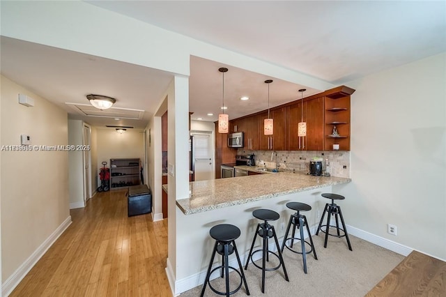 kitchen with tasteful backsplash, appliances with stainless steel finishes, a kitchen breakfast bar, kitchen peninsula, and pendant lighting