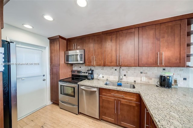 kitchen with appliances with stainless steel finishes, light stone countertops, sink, and decorative backsplash