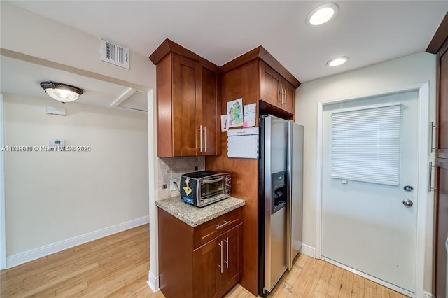 kitchen with light stone countertops, stainless steel fridge with ice dispenser, light hardwood / wood-style flooring, and decorative backsplash