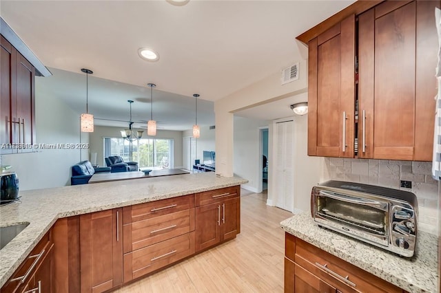 kitchen with light stone counters, decorative backsplash, pendant lighting, and light wood-type flooring