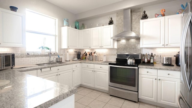 kitchen featuring appliances with stainless steel finishes, white cabinetry, sink, decorative backsplash, and wall chimney range hood