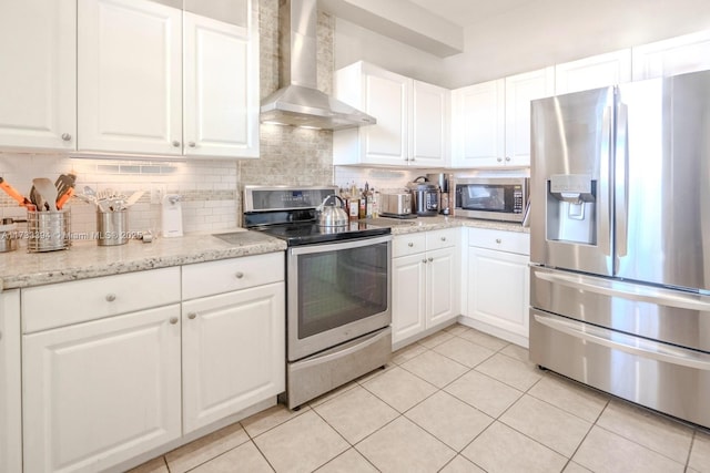 kitchen featuring light tile patterned floors, appliances with stainless steel finishes, white cabinetry, decorative backsplash, and wall chimney exhaust hood