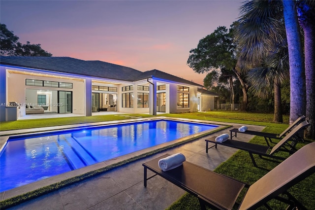 pool at dusk featuring a patio and a lawn