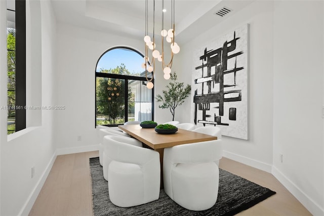 dining space with hardwood / wood-style floors, a raised ceiling, and a chandelier