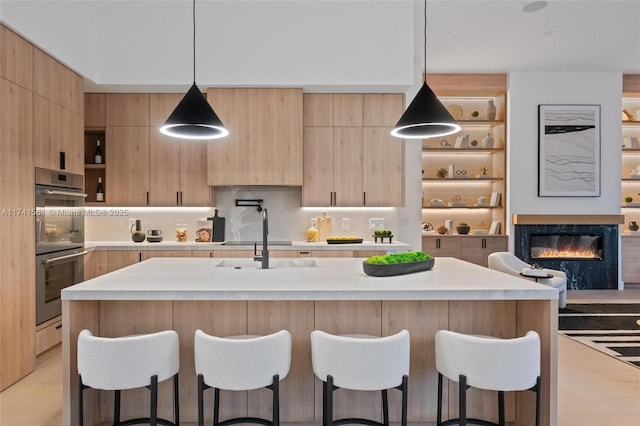 kitchen with an island with sink, stainless steel double oven, and decorative light fixtures