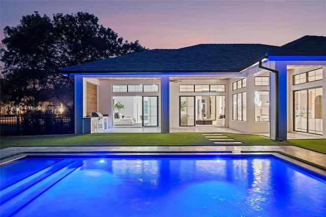 pool at dusk featuring a patio and a lawn