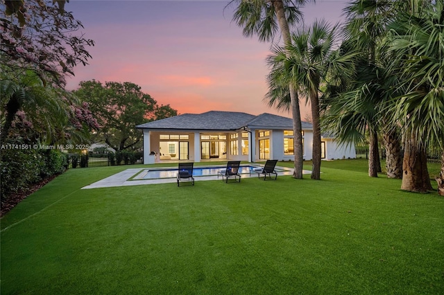 back house at dusk with a fenced in pool and a lawn