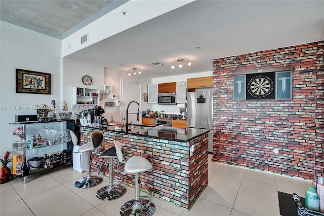 kitchen with sink, light tile patterned floors, appliances with stainless steel finishes, kitchen peninsula, and brick wall