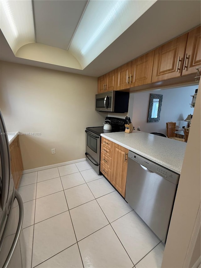 kitchen featuring appliances with stainless steel finishes, light tile patterned floors, and a tray ceiling