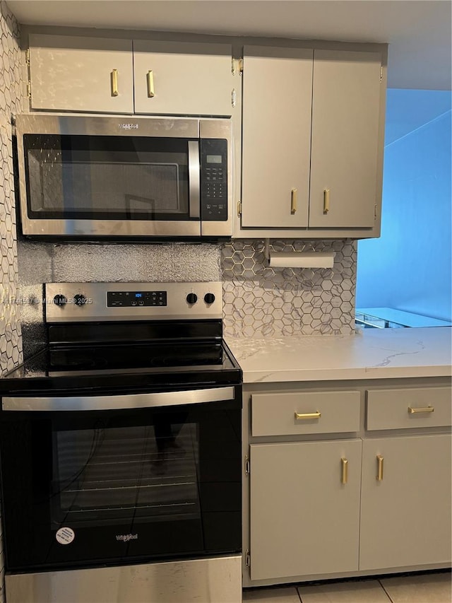 kitchen with light stone counters, backsplash, light tile patterned flooring, and appliances with stainless steel finishes