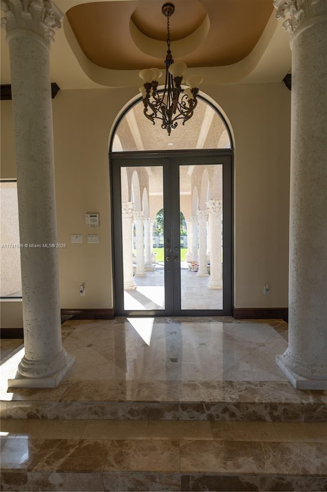 foyer featuring ornate columns, a high ceiling, a tray ceiling, an inviting chandelier, and french doors