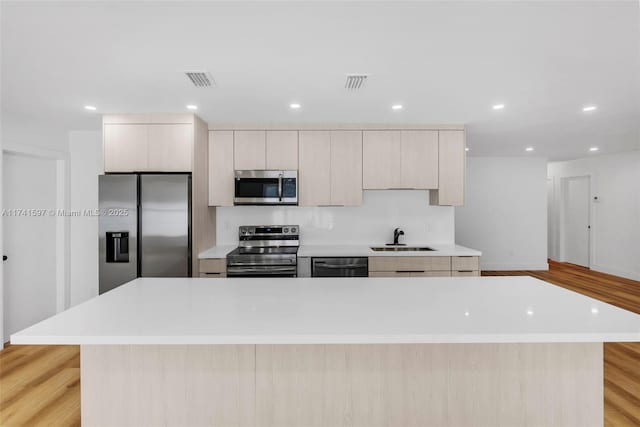 kitchen featuring stainless steel appliances, a center island, sink, and light wood-type flooring