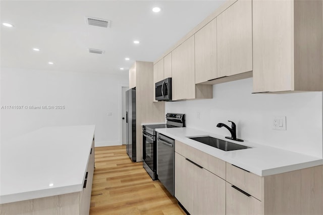 kitchen featuring light brown cabinetry, sink, light hardwood / wood-style floors, and appliances with stainless steel finishes