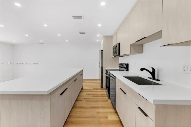 kitchen featuring stainless steel appliances, sink, light brown cabinetry, and light hardwood / wood-style flooring