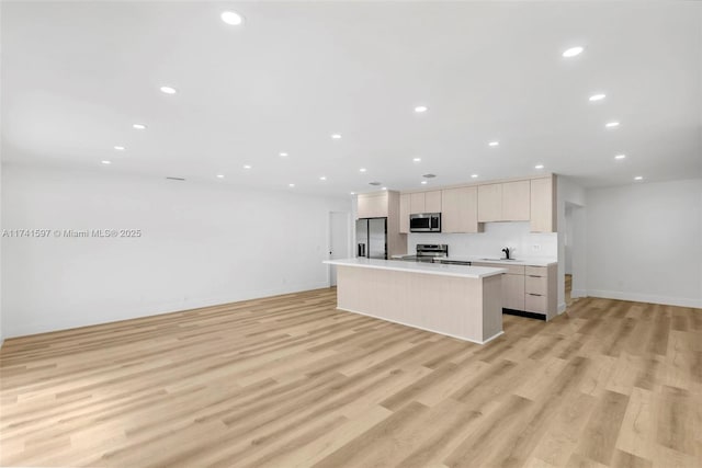 kitchen featuring light brown cabinetry, sink, appliances with stainless steel finishes, a kitchen island with sink, and light hardwood / wood-style floors