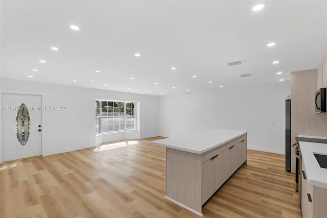 kitchen with light brown cabinets, stainless steel appliances, a kitchen island, and light hardwood / wood-style flooring