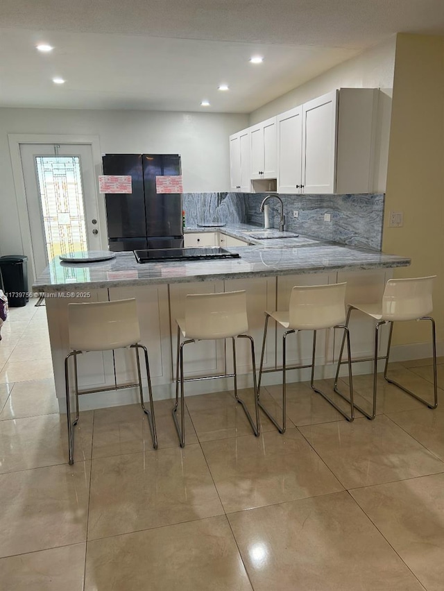 kitchen with black appliances, white cabinetry, a breakfast bar, and kitchen peninsula