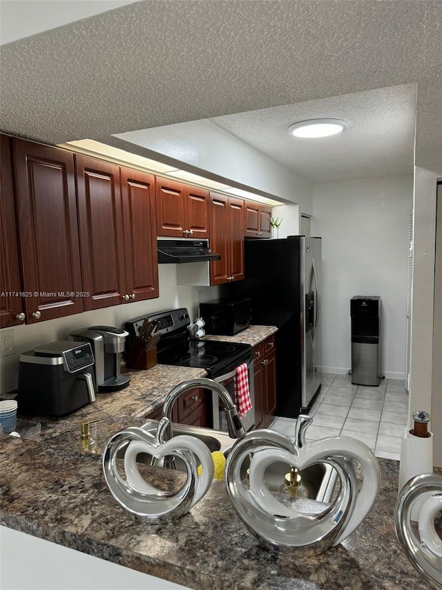 kitchen featuring stainless steel appliances, light tile patterned floors, a textured ceiling, and dark stone counters