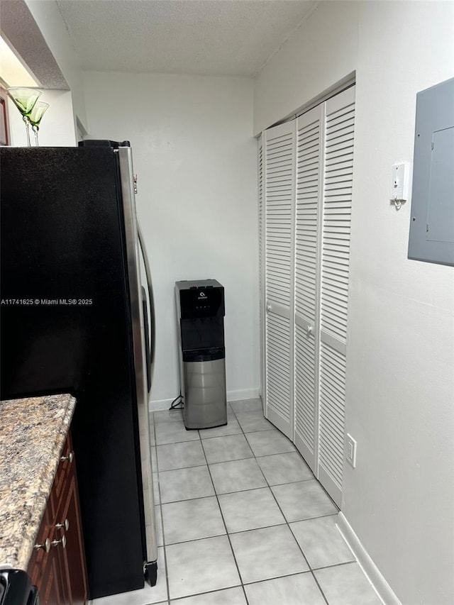 kitchen featuring stainless steel refrigerator, electric panel, a textured ceiling, and light tile patterned floors