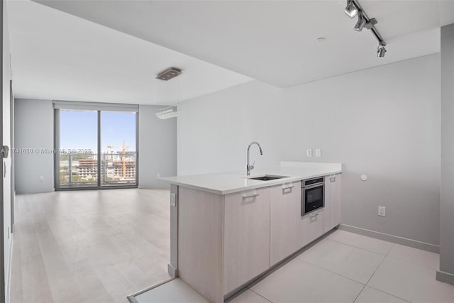 kitchen featuring oven, rail lighting, a wall of windows, light countertops, and a sink