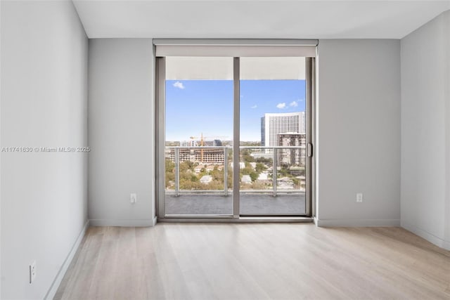 empty room featuring a view of city, a wall of windows, wood finished floors, and baseboards