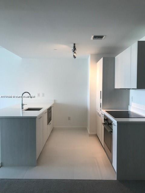 kitchen featuring black electric cooktop, sink, oven, and white cabinets