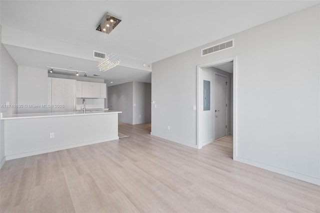 unfurnished living room with light wood-type flooring, electric panel, visible vents, and baseboards