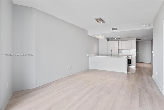 unfurnished living room featuring visible vents, a sink, light wood-style flooring, and baseboards