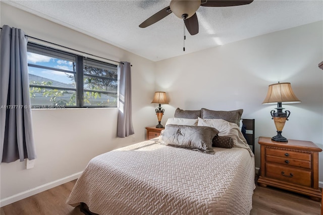 bedroom with ceiling fan, wood-type flooring, and a textured ceiling