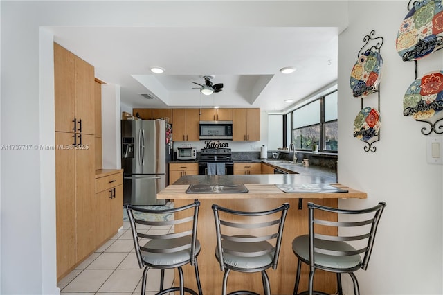 kitchen featuring sink, a breakfast bar area, stainless steel appliances, a tray ceiling, and kitchen peninsula