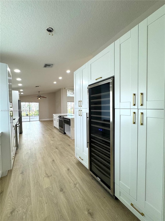 kitchen with beverage cooler, visible vents, light wood-style floors, white cabinetry, and open floor plan