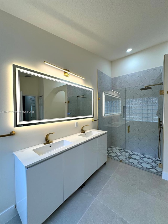 bathroom featuring double vanity, a stall shower, a textured ceiling, and a sink