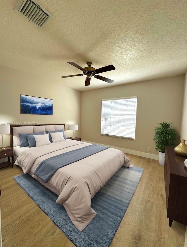 bedroom with visible vents, baseboards, light wood-style flooring, a textured ceiling, and a ceiling fan