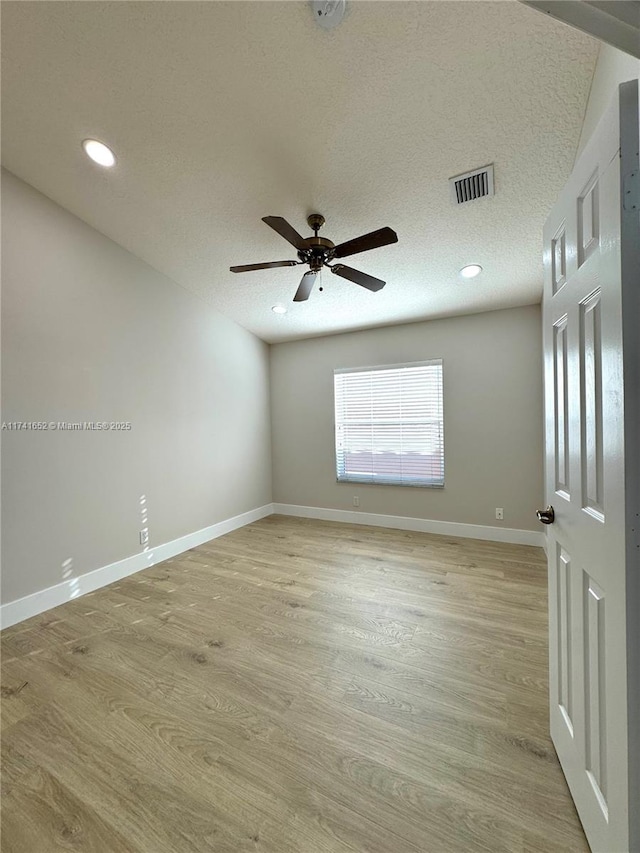 empty room with visible vents, baseboards, light wood-type flooring, and a textured ceiling