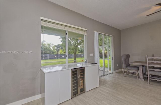 bar with a ceiling fan, beverage cooler, light wood-style flooring, and baseboards