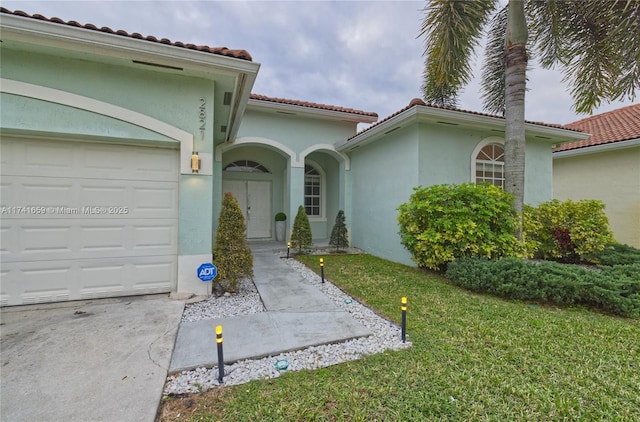 doorway to property featuring a garage, a lawn, a tile roof, and stucco siding