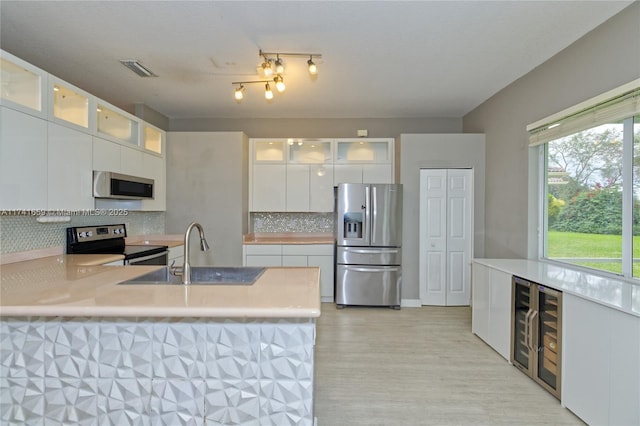 kitchen featuring beverage cooler, stainless steel appliances, a sink, white cabinets, and backsplash