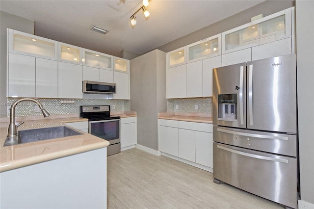 kitchen featuring backsplash, appliances with stainless steel finishes, white cabinets, a sink, and light wood-type flooring