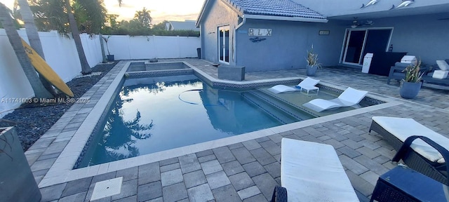 pool at dusk featuring a patio area and a hot tub