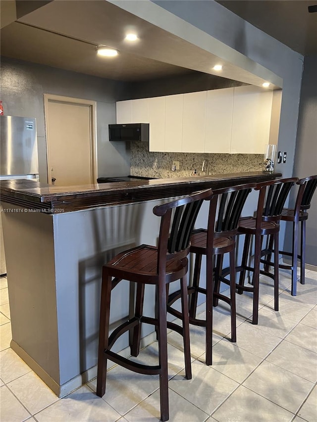 bar featuring light tile patterned flooring, white cabinetry, tasteful backsplash, ventilation hood, and stainless steel fridge